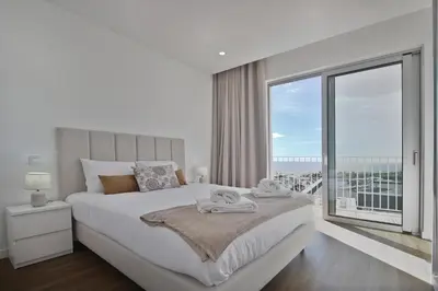 a white bedroom with a large bed and a large window at Like Home I - vista mar e ambiente relaxante in Funchal