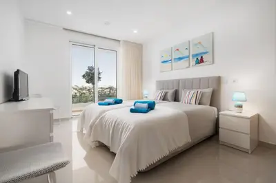 a white bedroom with a large bed with blue pillows at MaBelle Luxury Ocean View Apartment in Lagos
