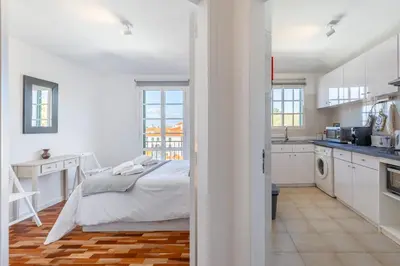 a white bedroom with a bed and a kitchen at Funchal pad with Harbor Views & cool Aircon Bliss in Funchal