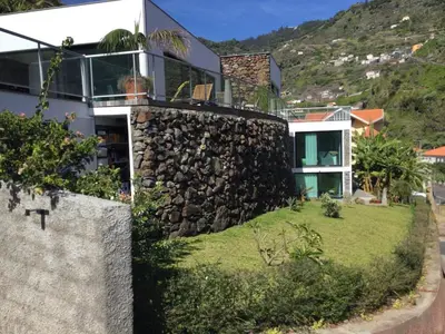 a house with a stone wall and a yard at Tabua Lodge in Ponta do Sol