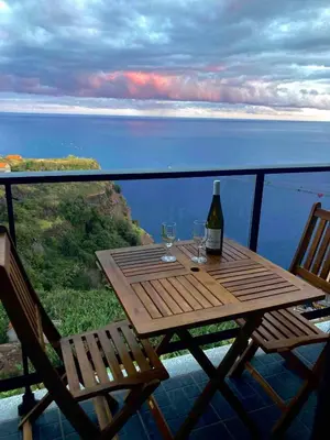 a wooden table with two glasses and a bottle of wine at Morning Glory Penthouse in Estreito da Calheta