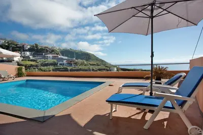 a swimming pool with an umbrella and a chair at Morning Glory 2 Bedroom Apartment in Calheta