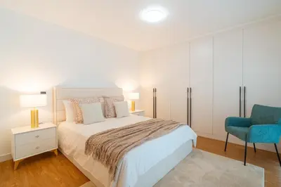 a white bedroom with a bed and a blue chair at Suite Q - Supermarket - Pool - AC - Private Parking Spot in Funchal