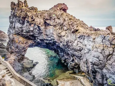 an arch in a rocky cliff next to the water at Pôr do Sol I in Porto Moniz