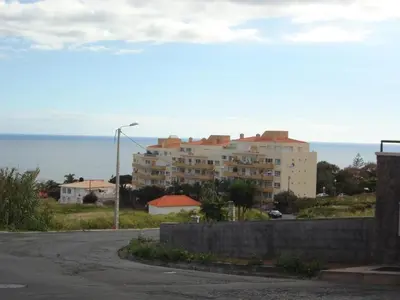 a building on a hill with the ocean in the background at Excellent Holiday Apartment in Caniço