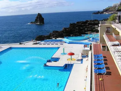 a pool with chairs and umbrellas and the ocean at Excellent Holiday Apartment in Caniço
