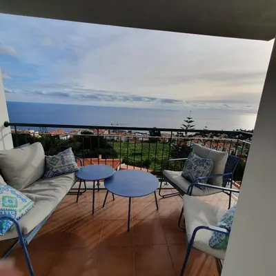 a balcony with a couch and tables and the ocean at Oceanview Getaway in Caniço