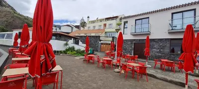 a group of red tables and chairs with red umbrellas at Casa Linda Baía in Porto da Cruz