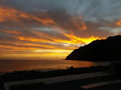 a sunset on the beach with the ocean and a mountain at Casa Linda Baía in Porto da Cruz