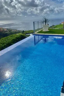 a large blue swimming pool with a view of the ocean at Vila Da Luz Calheta in Estreito da Calheta