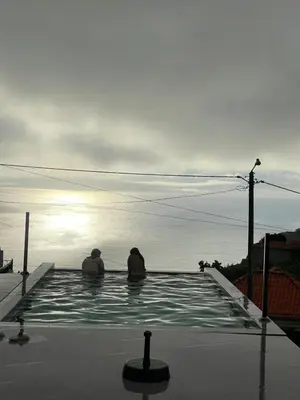 two people sitting in a swimming pool looking at the ocean at Sun Temple by Madeira Holiday Rentals in Ribeira Brava