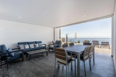 a dining room with a table and chairs and the ocean at Ocean and Palms in Arco da Calheta
