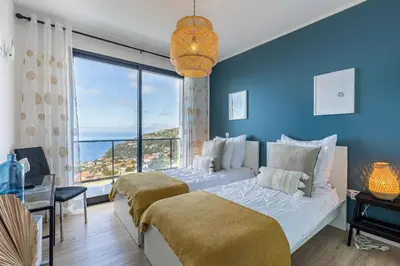 a blue bedroom with two beds and a large window at Ocean and Palms in Arco da Calheta