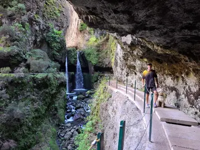 a man walking his dog on a path with a waterfall at Sally's Loft - Penthouse - Honeymoon suite in Ponta do Sol