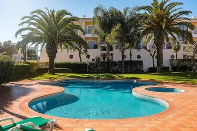 a swimming pool with palm trees in front of a building at Casa Clara Sun, Beach and Pool in Lagos