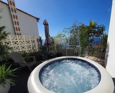 a hot tub on a patio with an umbrella at Villa Palmera Sea View in Arco da Calheta