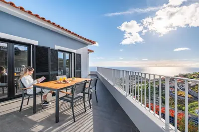 a woman sitting at a table on the balcony of a house at VIRA by KAAMAH in Estreito de Câmara de Lobos