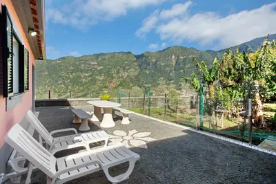 a patio with white chairs and a table with mountains in the background at Cristina Grand in São Vicente