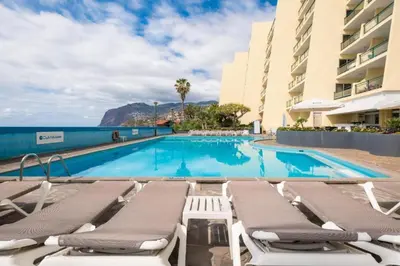 a swimming pool with lounge chairs and the ocean at Sunset Cove in Funchal