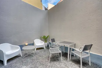 a patio with white chairs and tables and a wall at Mouraria Studios in Funchal