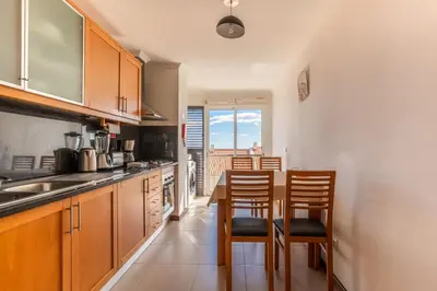 a kitchen with wooden cabinets and a table and chairs at Garajau View Apartment by Holiday Rental Madeira in Caniço