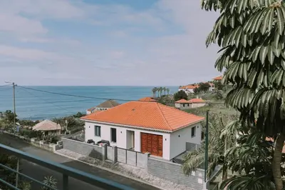 a white house with an orange roof and the ocean at Bela Vista House in Ponta Delgada