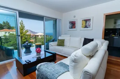 a living room with white furniture and a large window at Las Rosas Vista Baia do Funchal in Funchal