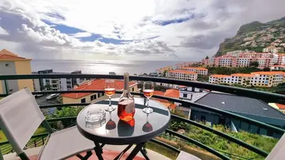 a table with two glasses of wine on a balcony at Perfume a Maresia in Câmara de Lobos