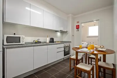 a kitchen with white cabinets and a table with chairs at Refúgio Girassol in Caniço