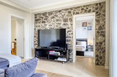 a living room with a stone wall with a television at Ricardo House, a Home in Madeira in Calheta