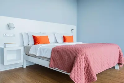 a white bed with orange pillows and a pink blanket at Casa da Lombada in Ponta do Sol