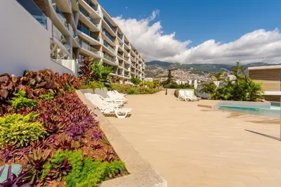 a building with white lounge chairs next to a swimming pool at GuestReady - The perfect place to relax in Funchal in Funchal