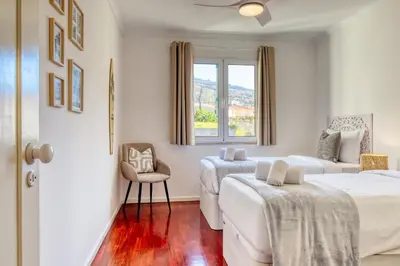a bedroom with two beds and a chair and a window at Funchal Panoramic View, a Home in Madeira in Funchal