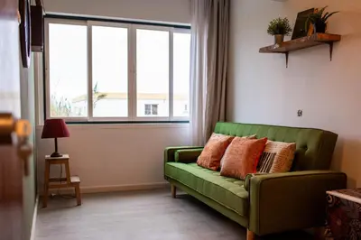 a green couch in a living room with a window at Seaview Ensuite rooms in Sagres centre - Casa Maluka in Sagres