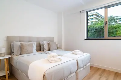 two beds in a white bedroom with a window at A peaceful retreat near the city centre in Funchal