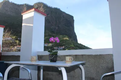 a table with two cups and a flower on a balcony at Leais ao Pico in Porto da Cruz