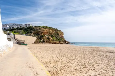a sandy beach next to the ocean with houses at Studio Sardinha-1 min walk to beach in Burgau