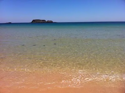 a beach with the ocean and a rock in the distance at Casa 3 in Raposeira