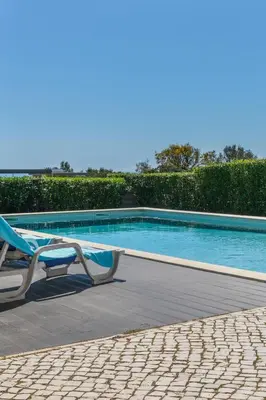 a swimming pool with a chair next to a hedge at Luz Home- Two Bedroom Villa in Luz