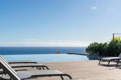 a pool with chairs and the ocean in the background at Savoy Monumentalis I by An Island Apart in Funchal
