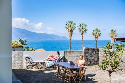 two people sitting on a patio with the ocean in the background at SUPER Sunset in Ponta Delgada