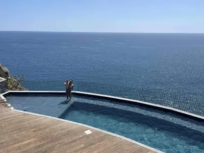 a man standing in a swimming pool overlooking the ocean at Oceanfront Elegance Madeira Retreat in Câmara de Lobos