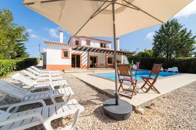 a villa with a pool and lawn chairs and an umbrella at Villa Azure Family & Surf Escape in Aljezur