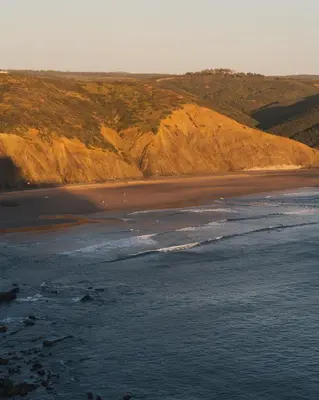 a beach with a group of people standing in the water at The Suites by The Lighthouse Arrifana in Aljezur
