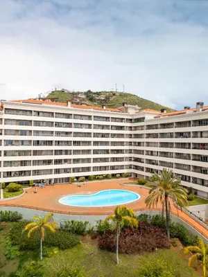 an apartment building with a swimming pool and palm trees at NÔNA Suite Funchal in Funchal