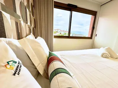 a bedroom with a bed with white sheets and a window at Colours by Madeira Best Apartments in Funchal