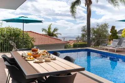 a table with breakfast food on it next to a swimming pool at Private pool and sea view - Tropical Villa in Arco da Calheta