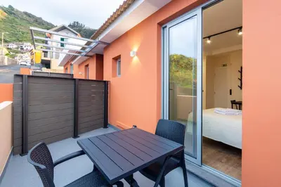 a balcony with a wooden table and chairs and a bedroom at The Jolie - Porto Moniz Central Studios in Porto Moniz