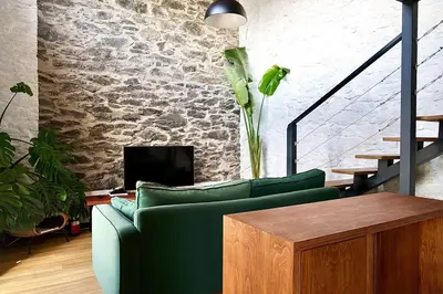 a living room with a green couch and a stone wall at NEW! Nature Paradise with Ocean View & Hot Tubs in Fajã da Ovelha