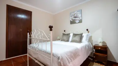 a bedroom with a white bed and a wooden cabinet at Marroas Cottage in Ponta do Sol